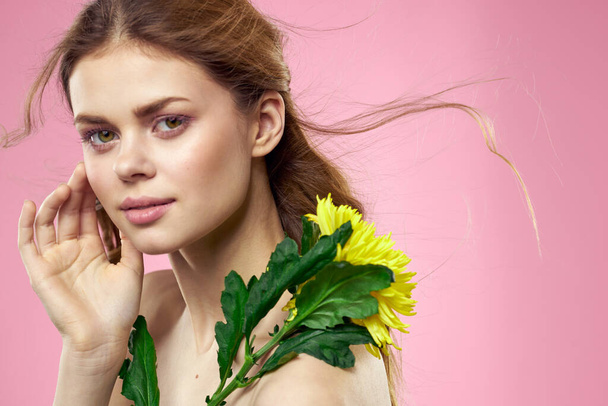 Krásná dívka se žlutou květinou na růžovém pozadí nahé ramena make-up - Fotografie, Obrázek