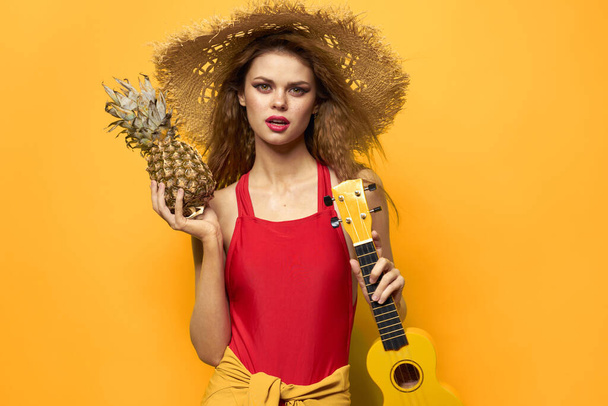 γυναίκα σε κόκκινο καπέλο ukulele στον τρόπο ζωής των χεριών καλοκαίρι κόκκινο t πουκάμισο κίτρινο φόντο - Φωτογραφία, εικόνα