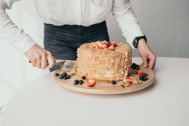 Ο ζαχαροπλάστης κόβει την τούρτα. Ένα νόστιμο κέικ μελιού κόβεται με μαχαίρι. Κοντινό πλάνο του κέικ μελιού - Φωτογραφία, εικόνα
