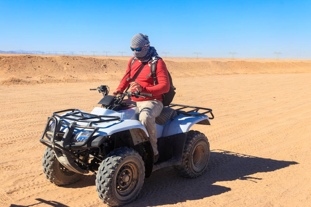 Молодий чоловік у сафарі подорожує через егіптську пустелю, їдучи на ATV. Quad bike safari in the Desert near Hurghada, Egypt - Фото, зображення