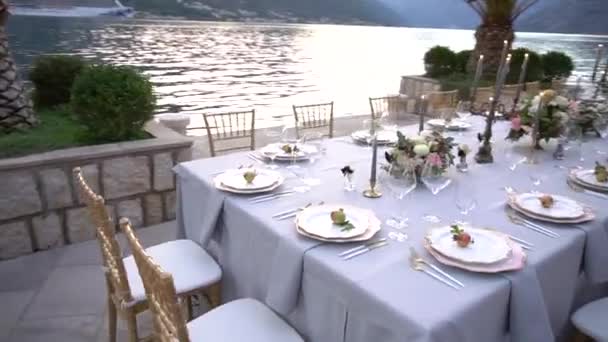 Stół na bankiecie weselnym, ozdobiony kwiatami, świecznikami i młodymi granatami na molo w Zatoce Kotor - Materiał filmowy, wideo