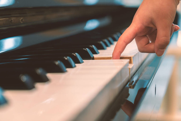 Jeden palec dziecka naciska na jeden klawisz fortepianu, widok perspektywy, który niski kąt i równolegle klawiatury fortepianu. - Zdjęcie, obraz