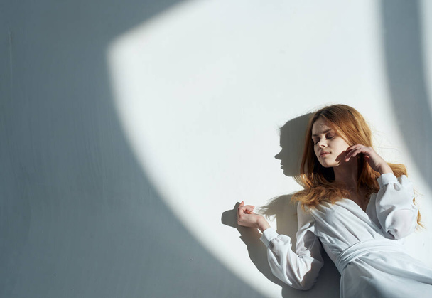 Mujer modelo se apoya contra la pared una sombra que cae de una habitación de vestido blanco - Foto, imagen