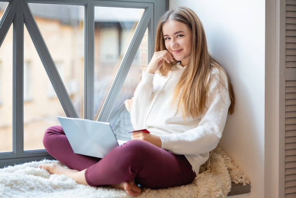 Una joven se sienta en la ventana y hace compras por Internet - Foto, Imagen