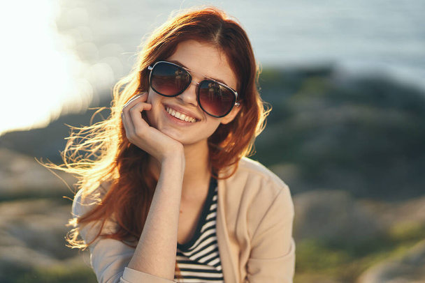 mujer feliz en gafas viaja por la naturaleza en las montañas cerca del mar y camiseta a rayas modelo suéter - Foto, imagen