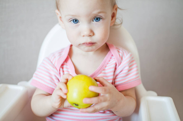 A little girl tastes, examines and plays with fresh apples with pleasure and interest. - Photo, Image