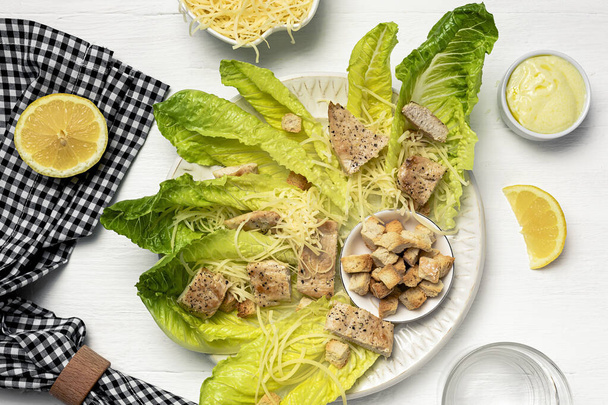 Homemade Caesar Salad with romanine, cheese, croutons, chicken, lemon and sauce. On white wooden background - 写真・画像