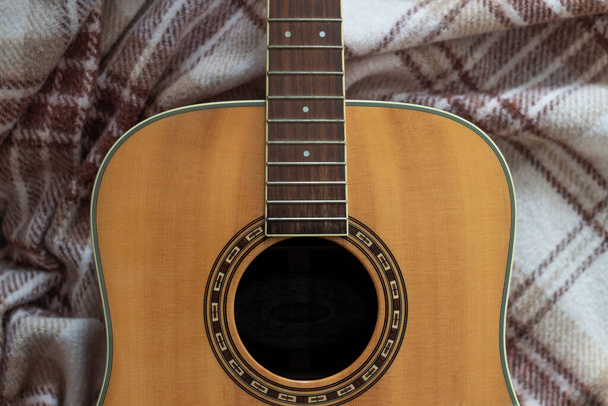 lehká dřevěná kytara bez provázků s černou dírou a hnědými vzory na vlněné hnědé kostkované kostkované - Fotografie, Obrázek