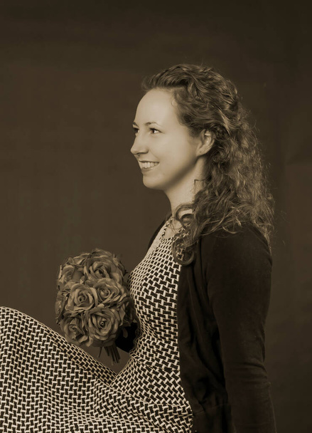 Retrato de joven hermosa mujer con ramo de flores de rosas. Sentada en un vestido y cabello rizado. En color marrón vintage foto. Vintage, estilo retro de 1900 - Foto, imagen