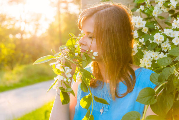 Portrait of beautiful blonde hair woman inhales the fragrance of spring flowers of blooming jasmine tree - Fotó, kép