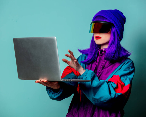 Stílusos lány cyber punk szemüveg és 80-as évek melegítő hold laptop számítógép kék háttér - Fotó, kép