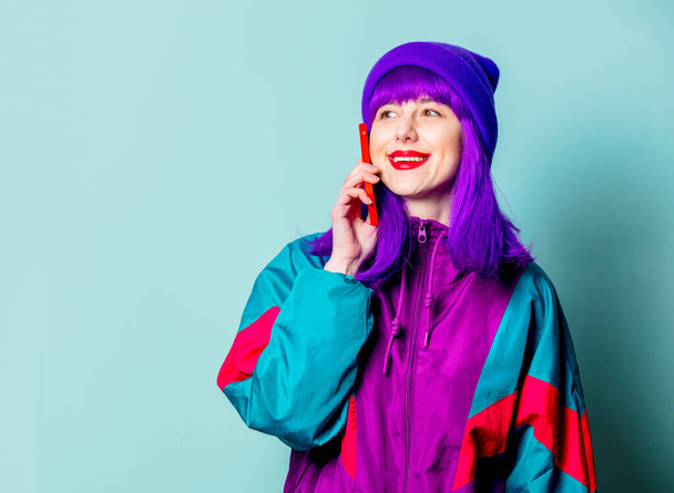 Tyylikäs valkoinen tyttö violetti hiukset ja 80-luvun verkkarit matkapuhelimella sinisellä taustalla - Valokuva, kuva