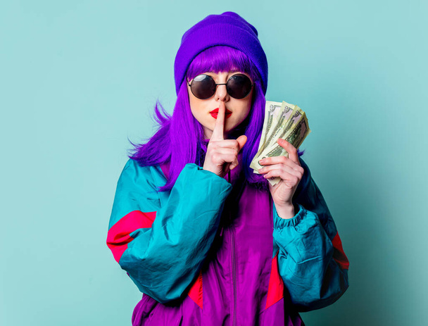 Tyylikäs valkoinen tyttö violetti hiukset ja 80-luvun verkkarit pitää käteistä rahaa sinisellä pohjalla - Valokuva, kuva