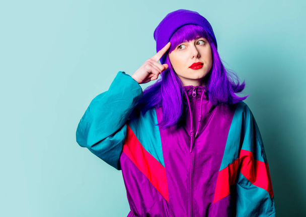 Surprised white girl with purple hair and 80s tracksuit point finger on her head on blue background - Photo, Image