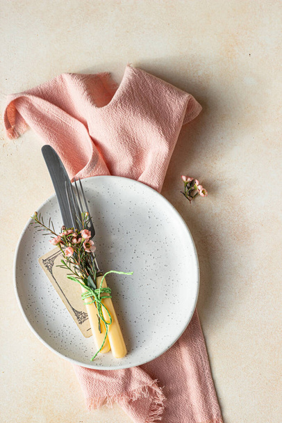 Romantic or spring table setting. Knife and fork, little pink flowers and linen napkin on a plate, light concrete background. Flat lay. Selective focus. - Foto, afbeelding
