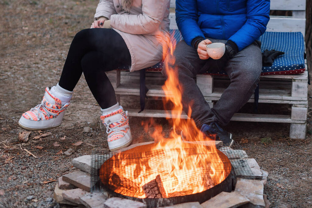 Two friends are sitting around a campfire and relaxing, backpackers relaxing near campfire, tourist background. - Photo, Image