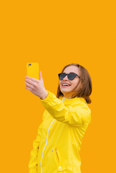 Retrato de chica atractiva en ropa de verano toma selfie sobre fondo amarillo, mira a la cámara y sonríe - Foto, imagen