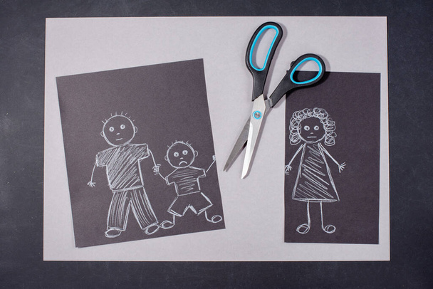 Lapsen piirustus perheestä paperilla mustalla taustalla. Äiti, isä ja vauva pitävät toisiaan kädestä. Perhe-avioeron käsite. Äidin kuva on leikattu saksilla. Suhteen ongelmat ja vaikeudet  - Valokuva, kuva