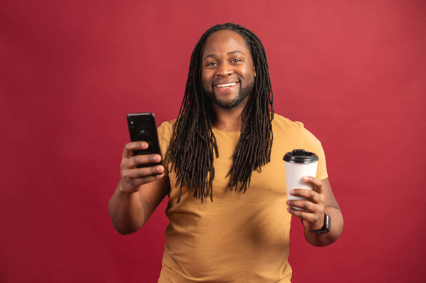 Photo of cheerful black man using smartphone and takeaway cup - Foto, afbeelding