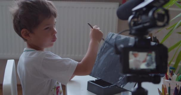 Blogger ragazzo dipinge opere d'arte su tela guardando nella fotocamera - Filmati, video