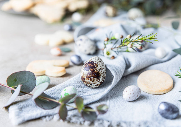 Easter cookies with candies shaped eggs, floral decor and quail eggs on linen napkin, stone background. Holiday concept. Selective focus. - Fotografie, Obrázek