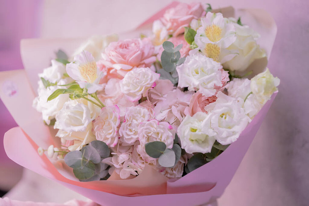 Ein üppiger Strauß von zartrosa, weißen, zarten Rosen in verschiedenen Größen, Blüten aus grünen Blättern. Papierverpackungen. Romantik. - Foto, Bild