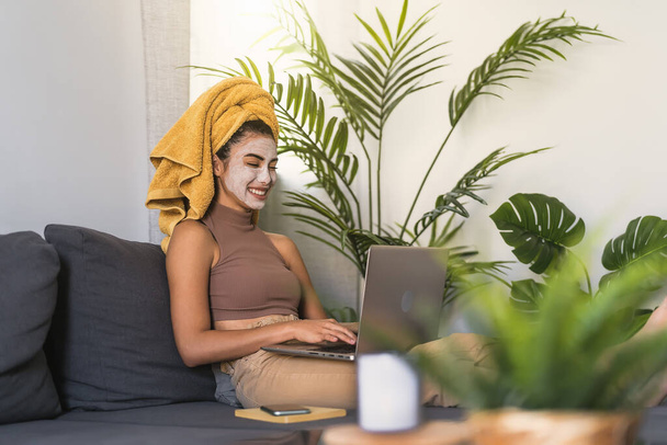 Młoda kobieta korzystająca z laptopa podczas dnia pielęgnacji skóry w domu - Zdjęcie, obraz