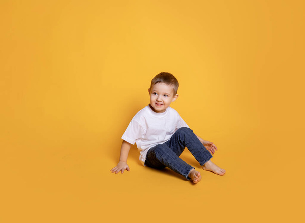 niño pequeño en jeans y una camiseta blanca sobre un fondo amarillo - Foto, Imagen