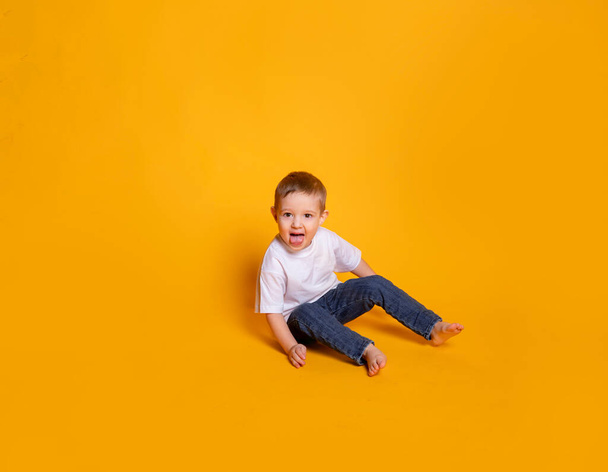 little child in jeans and a white t-shirt on a yellow background - Photo, Image