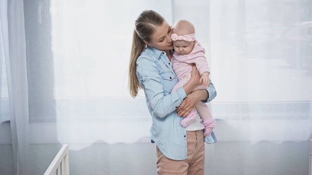 woman holding in arms infant daughter in headband with bow - Valokuva, kuva