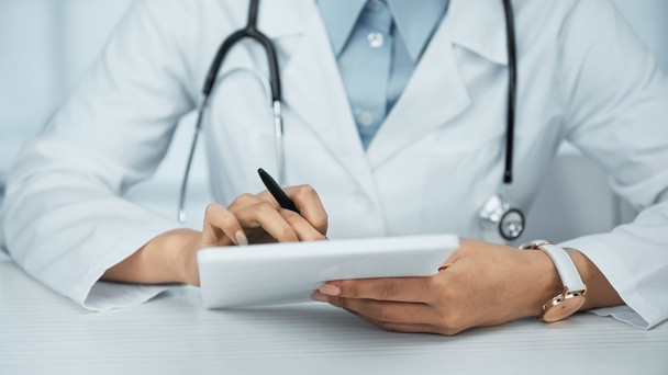 Teilansicht eines afrikanisch-amerikanischen Arztes im weißen Kittel mit digitalem Tablet  - Foto, Bild