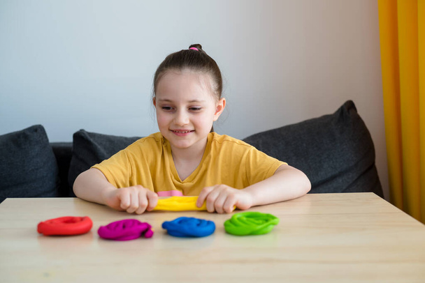 A preschool girl in a yellow T-shirt with a rainbow sculpts from plasticine at home. Quarantine activities for children. - Photo, Image