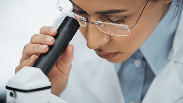 Gözlüklü Afrikalı Amerikalı bilim adamı mikroskoptan bakıyor.  - Fotoğraf, Görsel