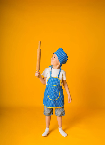 small boy in a chef's suit holds a rolling pin on a yellow background with a place for text - Fotografie, Obrázek