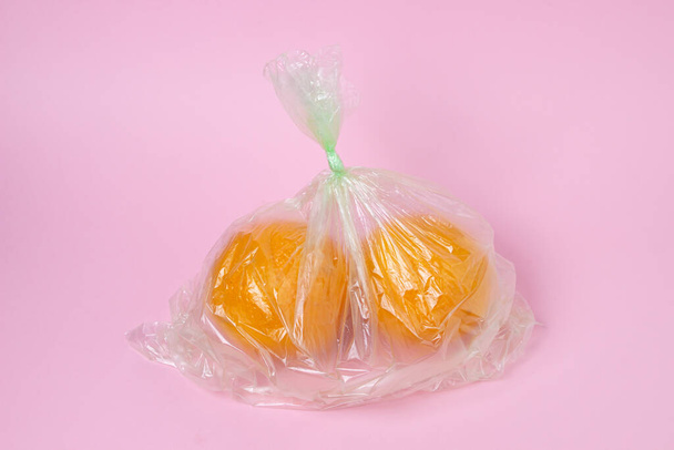 Апельсины в пластиковом пакете на розовом фоне. Апельсины на светлом фоне. Покупка апельсинов - Фото, изображение