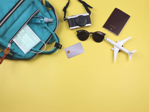 Top view or flat lay of traveling accessories with medical face mask and alcohol  spray in backpack on yellow background. Traveling during covid-19 and new normal. - Photo, Image