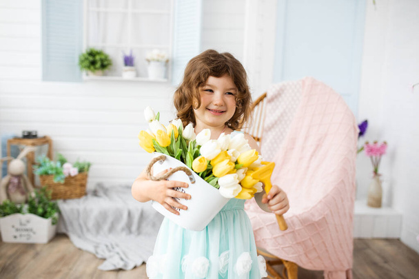 Photo of beautiful smiling girl 4-5 years old with yellow tulips on background of white veranda in studio - Fotó, kép