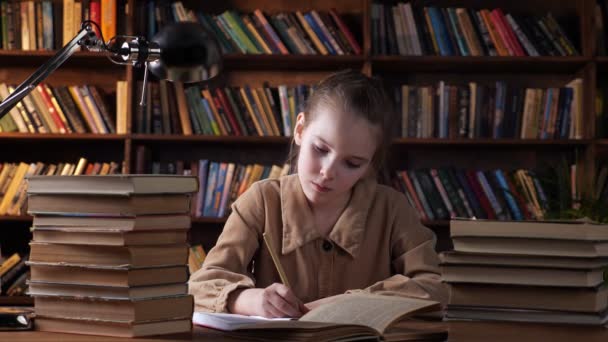 Κουρασμένη νεαρή κοπέλα με καφέ σακάκι γράφει υλικό από το βιβλίο - Πλάνα, βίντεο