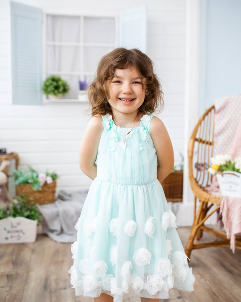 Портрет дівчини 4-5 років посміхаючись і дивлячись в рамку на тлі білого заднього двору
 - Фото, зображення
