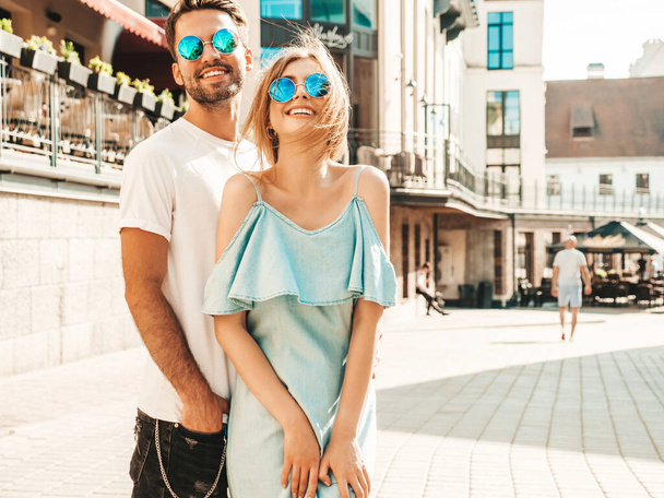 Portrait of smiling beautiful woman and her handsome boyfriend. Woman in casual summer jeans dress. Happy cheerful family. Female having fun. Couple posing on the street background in sunglasses - Valokuva, kuva