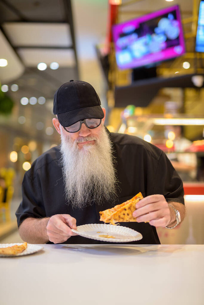 Vertical shot of man sitting in shopping mall and eating pizza - Φωτογραφία, εικόνα