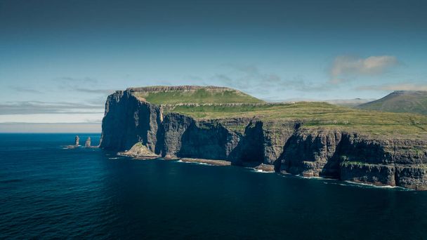 Скальные образования Risin og Kellingin на Фарерских островах в течение дня с солнцем и голубым небом, голубым океаном и зелеными скалами - Фото, изображение