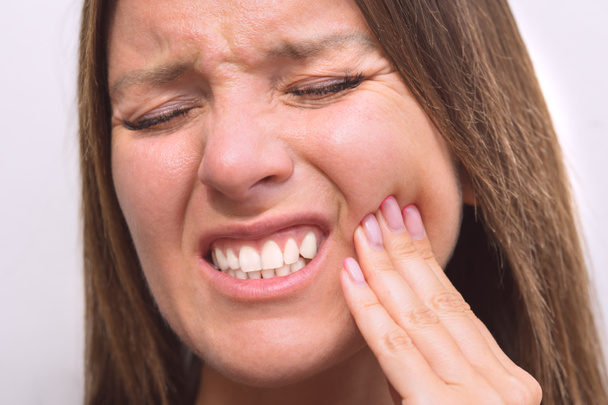 Женщина касается щеки из-за зубной боли. Женщина, страдающая зубной болью, стоматологическими заболеваниями или заболеваниями полости рта. Крупный план женского лица с болезненным выражением лица. Проблемы с зубами. Женщина чувствует зубную боль - Фото, изображение