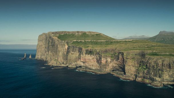 Vista panorâmica na costa da ilha Eysturoy com formações rochosas Risin og Kellingin nas Ilhas Faroé durante o dia com sol e céu azul, oceano azul e falésias verdes - Foto, Imagem