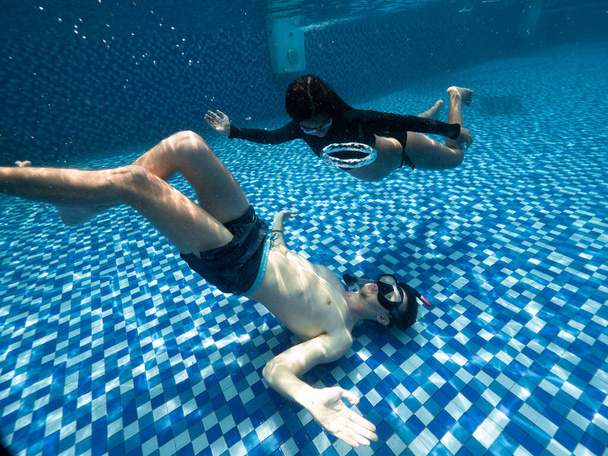 Underwater view in pool of a young woman and man on a summer day. - Photo, Image