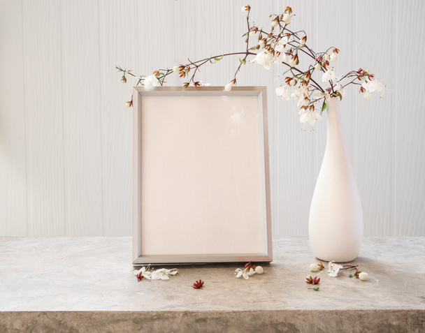 Marco de imagen de maqueta en blanco y flor seca en jarrón de vidrio y hermosas flores de Clerodendron asintiendo en jarrón moderno establecido en mesa de hormigón con fondo de madera blanca - Foto, imagen