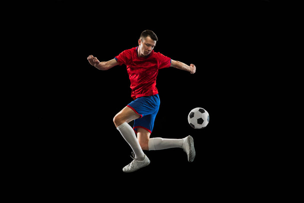 Young Caucasian soccer football player practicing isolated on black background. - Foto, Imagen