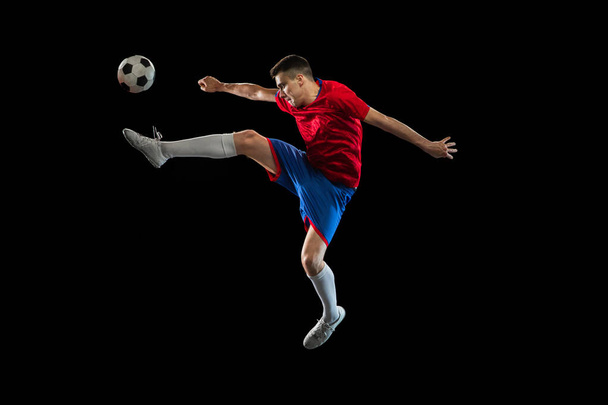Young Caucasian soccer football player practicing isolated on black background. - Photo, Image