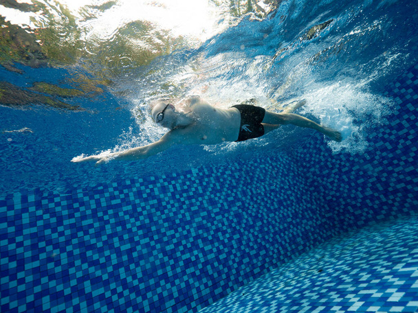 A Caucasian man in short and goggle swimming in the blue swimming pool outdoor - Photo, Image