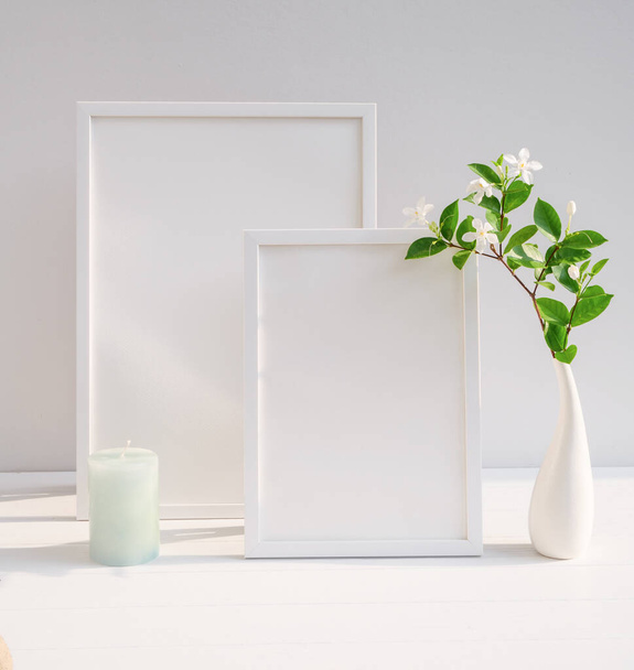 Vyhonit plakát bílý rám a krásné Gardenia tropické květinové v moderní bílé vázy dekor se zelenou svíčkou na béžový stůl a betonové stěny pozadí s dlouhým stínem - Fotografie, Obrázek